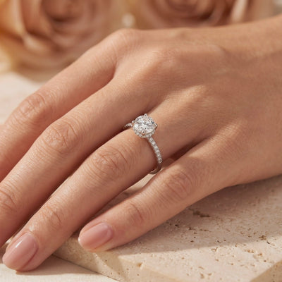 Silver ring with a round clear center stone and micro-pavé shoulders, worn on a person's hand.
