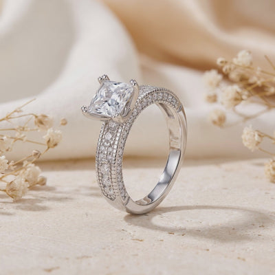 Three-quarter view of a silver ring standing upright, showing its raised square-cut setting and pavé band.