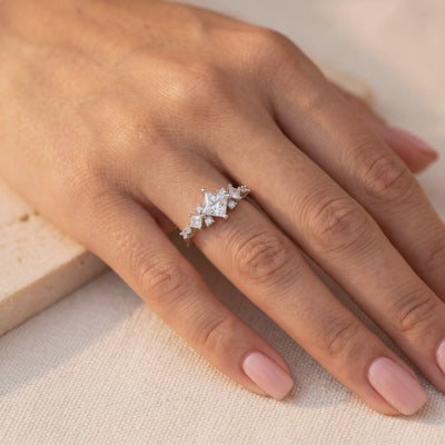 On-model hand view of a silver ring with a kite-set princess-cut center stone.