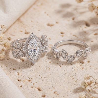 Silver marquise-cut ring beside its leaf-motif contour band on a textured stone surface.
