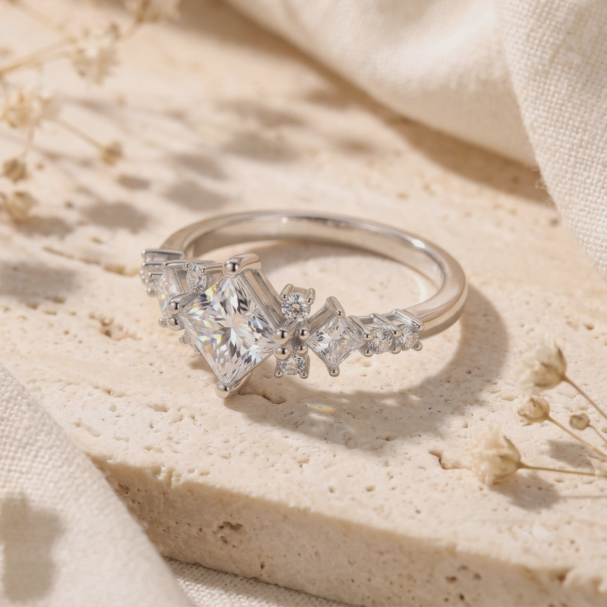 Silver ring with a kite-set princess-cut clear stone on a textured cream surface.