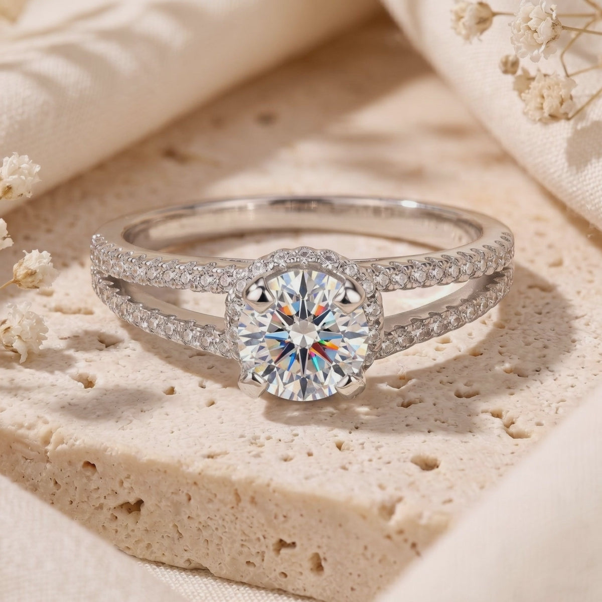 Close-up of a silver ring with a round clear center stone and pavé split-shank band on a textured stone surface.