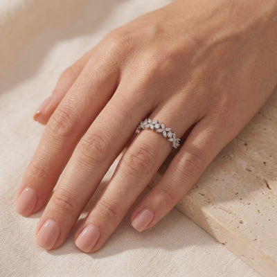 Silver floral cluster ring with marquise stones worn on a hand resting over textured beige fabric.