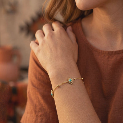 Gold-tone sunburst chain bracelet with turquoise-color accents, shown worn on a wrist
