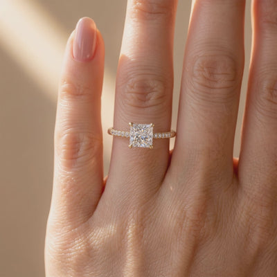 Gold-tone pavé solitaire ring with a princess-cut center stone worn on a finger, viewed from above.