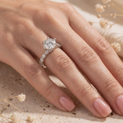 Silver-colored ring worn on a hand, with a round clear center stone, six-prong setting, and accent stones along the band.