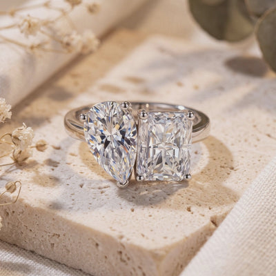 Silver Corentine Toi et Moi ring with pear- and radiant-cut stones displayed on a beige stone slab