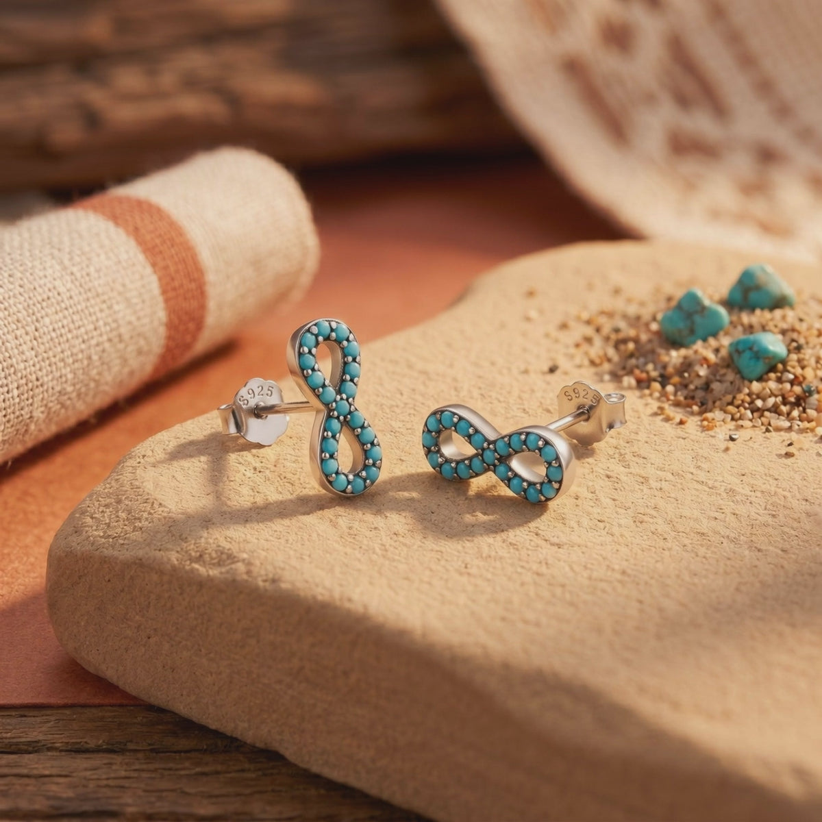 Pair of silver infinity stud earrings with turquoise stones and post backs on a tan display slab.