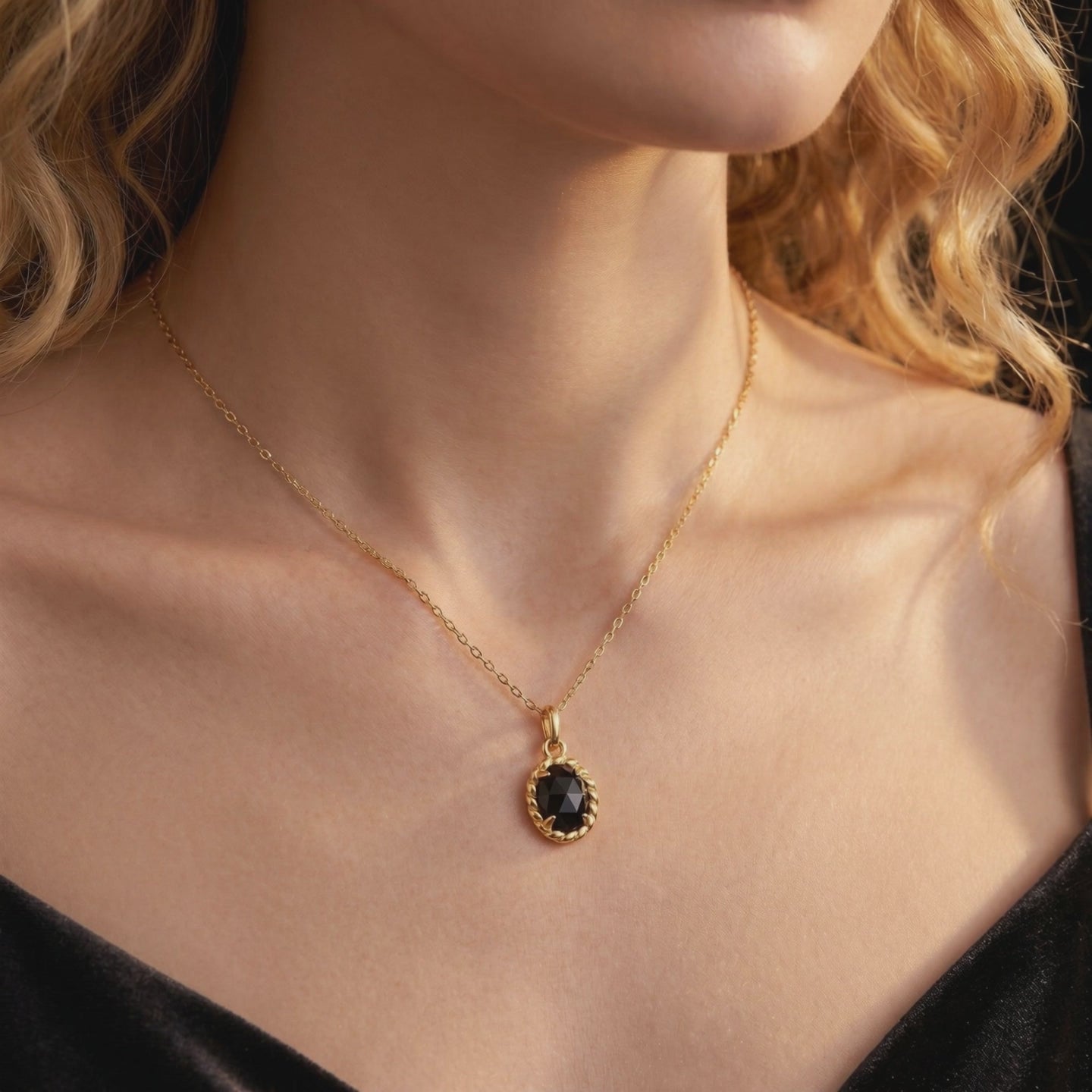 Model wearing a solid gold necklace with an oval black onyx pendant in a twisted border setting.