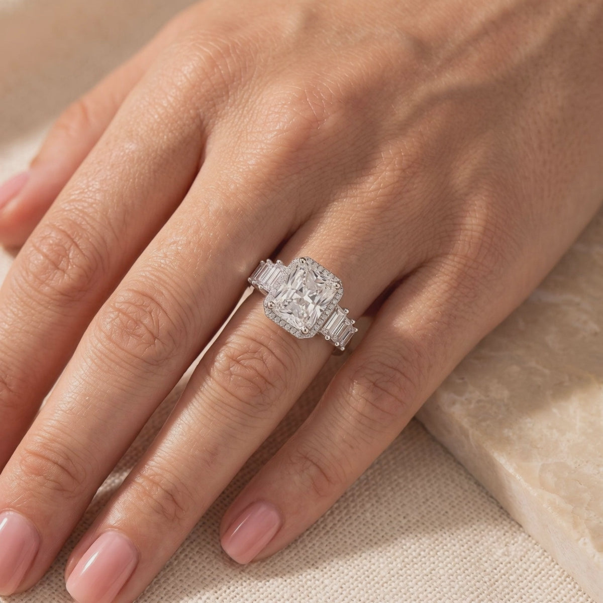 Silver cushion-cut halo ring with baguette accents worn on a ring finger
