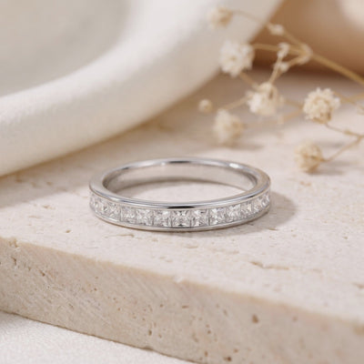 Close-up of a silver princess-cut channel-set eternity ring resting on a textured beige surface