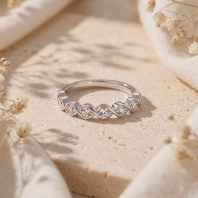 Silver twist wave ring with bezel-set clear stones resting on a textured cream-colored surface.