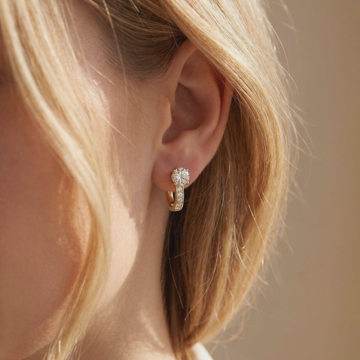 Gold-toned hoop earring with a round moissanite center and smaller accent stones, worn on an ear.