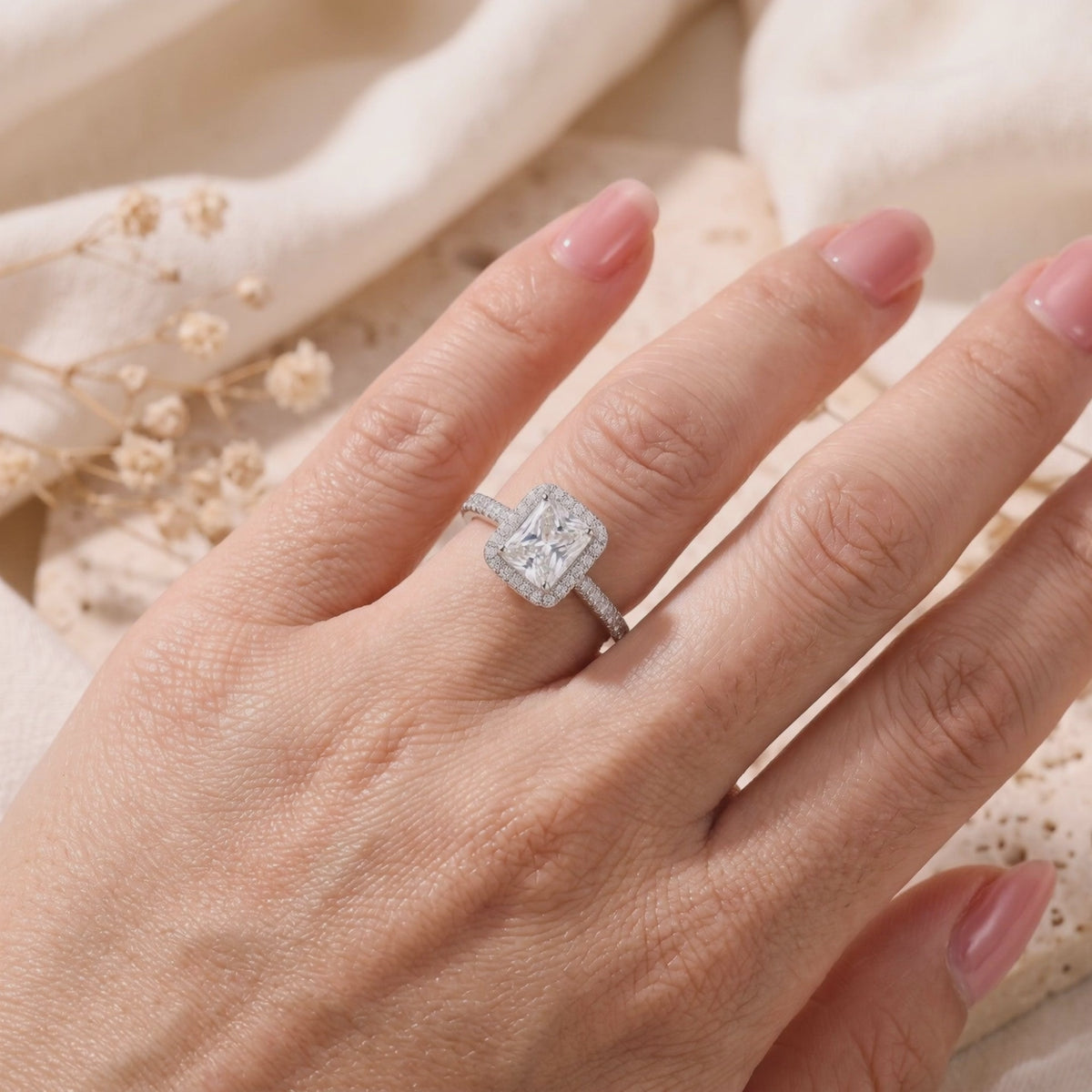 Silver radiant-cut halo ring with pavé band, worn on a hand over a textured background.