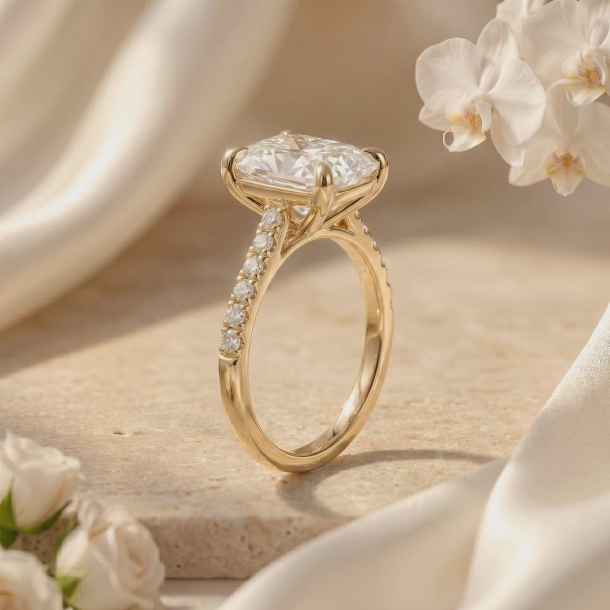 Side-profile view of a gold-tone cushion rectangular pavé solitaire ring beside white flowers.