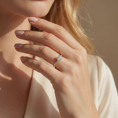 Close-up of a hand wearing a round-cut moissanite solitaire ring with a pavé band near the face.